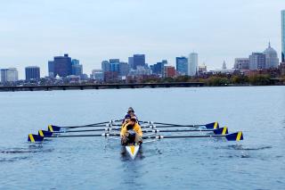 The Simmons crew team rowing with the Boston skyline behind them