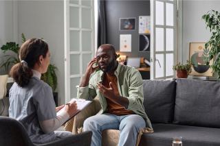 A social worker seated in a chair speaking to a client who is seated on a couch