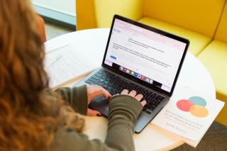 A student at a round table using a laptop with an open notebook on the table