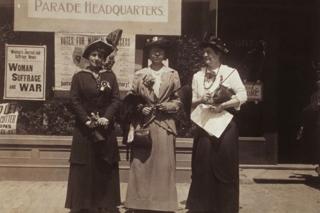 Three women standing in front of the parade headquarters of the Massachusetts Woman Suffrage Association, 1914