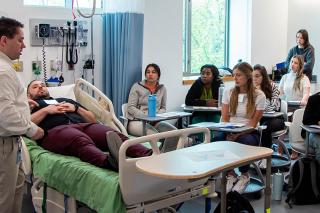 Nursing Students in classroom featuring practice patient in hospital bed