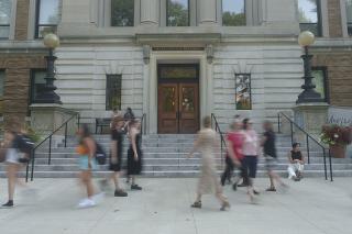 Various people walking by MCB main entrance. One person sitting on steps.