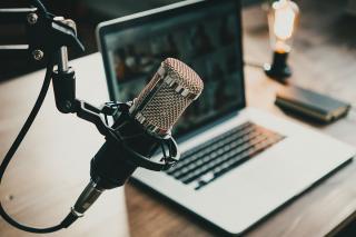 A home podcast studio with laptop, microphone, and lightbulb signalling live audio