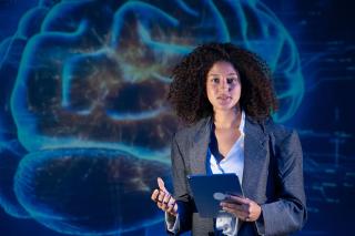 A woman making a presentation with a brain displayed on the wall behind her