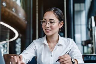 A woman with one hand on the keyboard of a laptop and the other hand holding a pen