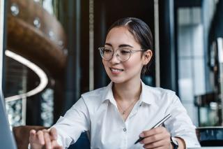 A woman with one hand on the keyboard of a laptop and the other hand holding a pen