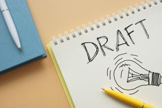 A spiral pad with the word "DRAFT" on it along with a hand drawn picture of a lightbulb