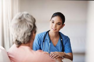 A healthcare worker holding a patent's hand and listening intently.