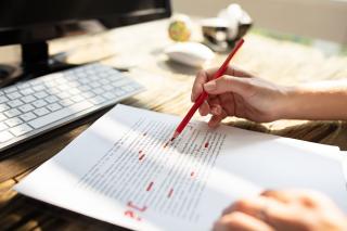 Close up of a person editing a printed paper with a red pen