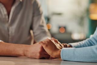 Two people holding hands for comfort across a table