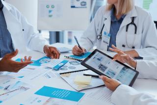 A number of healthcare workers at a table covered with pamphlets and papers.  One of them is using a tablet.