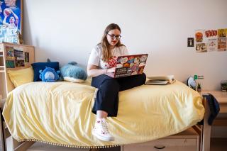 A Simmons student sitting on a bed in one of the student rooms in the new Living-Learning Center at Simmons University