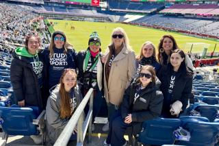A group of Simmons students with Dean Astrid Sheil and others wearing "Study Women's Sports" shirts at a Legacy soccer game.