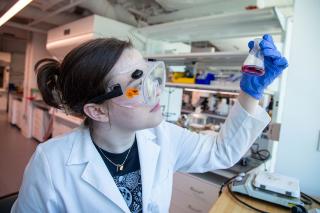 A Simmons student wearing goggles and working in the chemistry lab