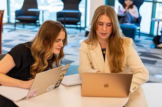 Two students working together on laptops in library