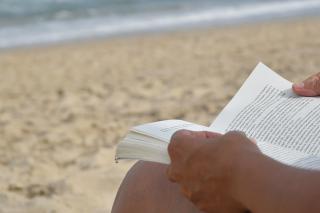 Hands of person holding book on beach. Photo by Pedro Fleitas.