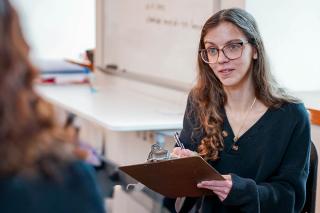 A student holding a clipboard talking to another student