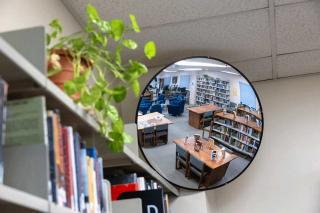 A bookshelf containing books and a plant as well as a round mirror that is reflecting a room in the library. Photo courtesy of the Colorado State Library – Colorado Department of Education