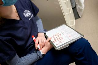 A closeup of a nursing student with a notebook on their lap in which they are taking notes
