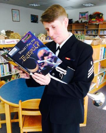 Vin Sowders in a library reading a book entitled "Should I Play the Trumpet?"