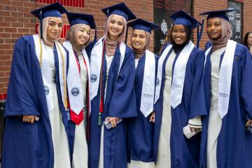 6 Simmons students wearing caps and gowns adorned with white stoles as they await the start of Commencement 2025
