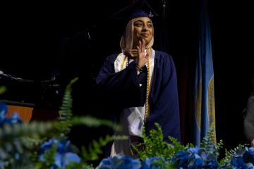 A graduating student waves as they cross the stage during Commenement 2025