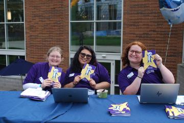 Orientaiton 2025 - Three Leaders holding up this year's programs at a check in table