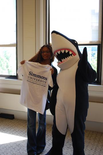 Orientation 2025 - A student holding up a Simmons t-shirt, posing for photo with Stormy