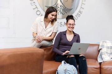 Two Simmons students looking at a laptop while seated in a student lounge