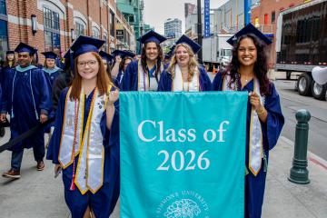 Graduates in the class of 2026 carry their class banner into Commencement
