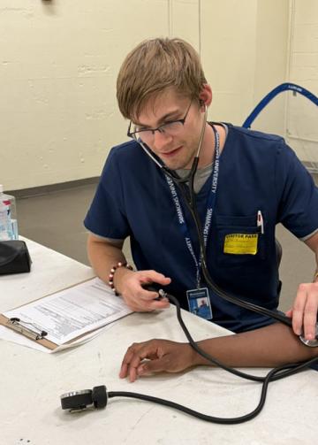 Clif Ricciardi '29 direct entry MSN RN-FNP takes a student's blood pressure at Fenway High School. 