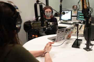 Students sitting in radio studio, wearing masks, talking into microphones