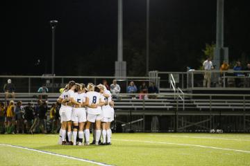 Simmons Soccer Team in huddle on field at night game