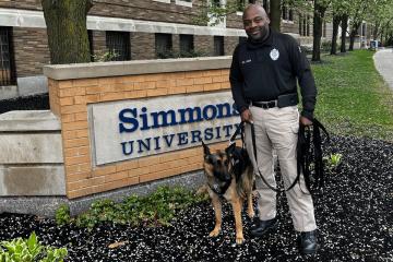 Athena, the Simmons Police comfort dog, with Detective Melvin Detective Ligon by the street side Simmons sign