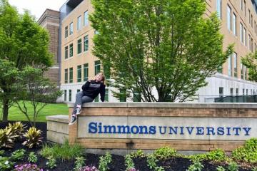 Alum Georgia Harper ’22 sitting on Simmons corner sign