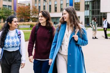 Three smiling Simmons students walking together through the Main Campus Quad