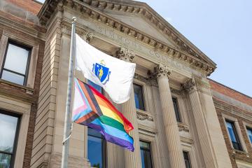 Pride Flag flying with MA state flag in front of Simmons MCB