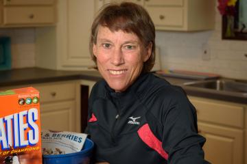 Nancy Clark seated at a kitchen table with a box of Wheaties cereal