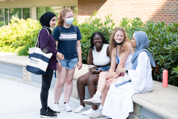 A group of Simmons students having a conversation while some are seated on a low patio wall