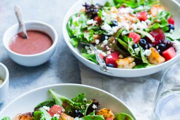 Two bowls of salad with dressing in bowls on the side. 