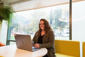 A Simmons online student working at a laptop in front of a picture window.