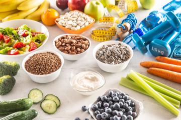 A collection of nutritious foods such as nuts, fruits, and vegetables alongside a set of weights and a jump rope