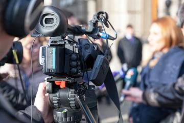 Close-up of a video camera being operated at an outdoor speaker event