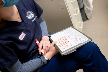 A closeup of a nursing student with a notebook on their lap in which they are taking notes