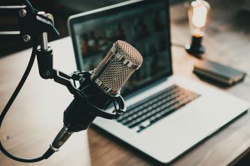 A home podcast studio with laptop, microphone, and lightbulb signalling live audio