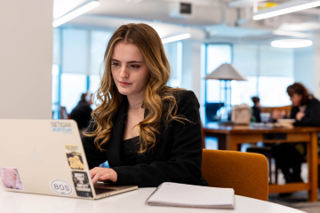 A Simmons student working on a laptop in a library