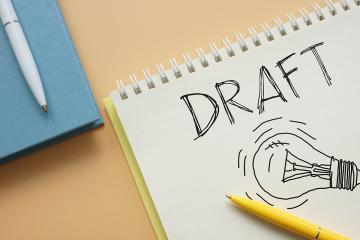 A spiral pad with the word "DRAFT" on it along with a hand drawn picture of a lightbulb
