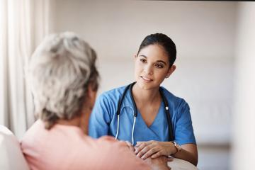 A healthcare worker holding a patent's hand and listening intently.