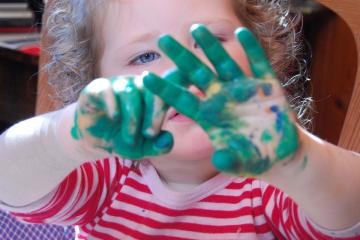 A small child holding up hands with green paint all over them