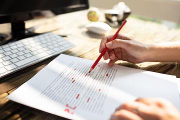 Close up of a person editing a printed paper with a red pen